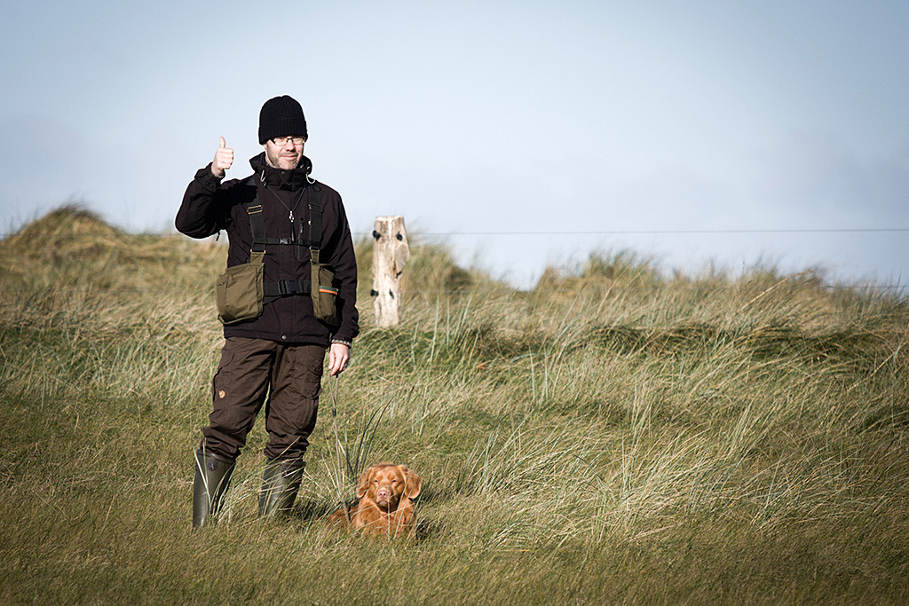 Edison liegt tiefenentspannt neben Stephan im hohen Gras, der die Geste »Daumen hoch« macht