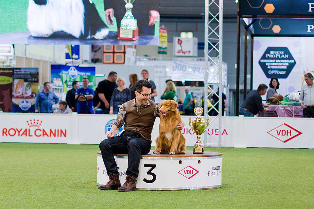 Edison sitzt zusammen mit Stephan und dem Pokal auf dem Podest für den dritten Platz, beide strahlen