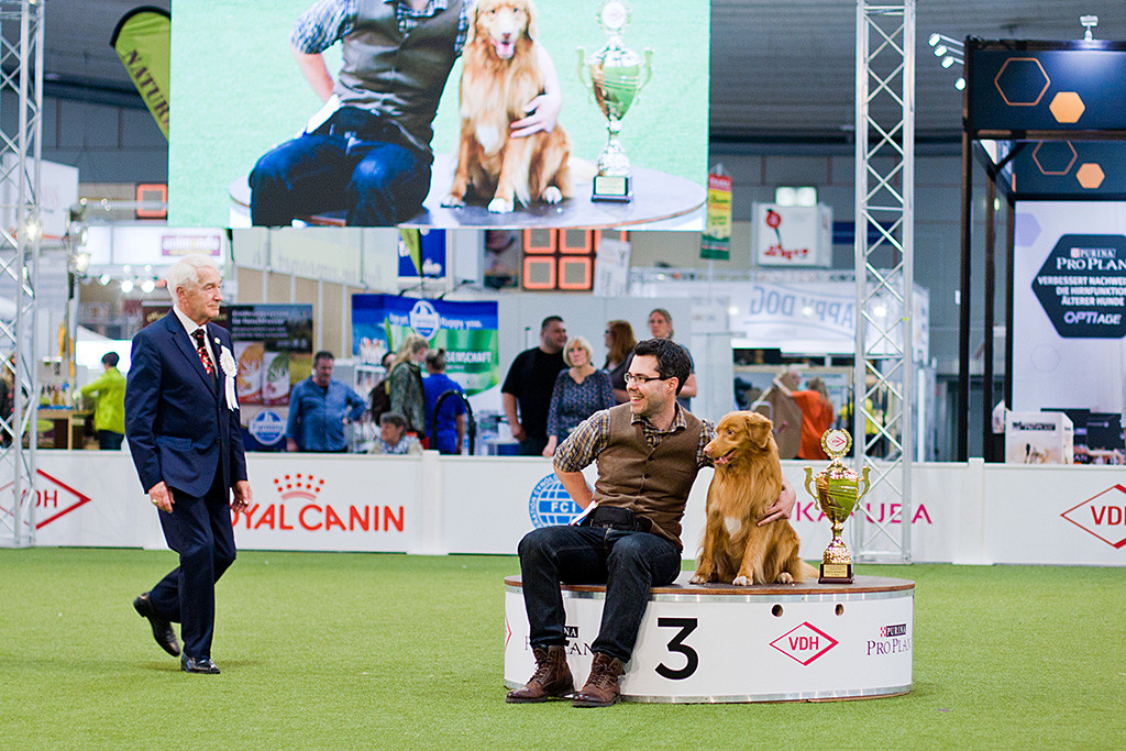 Edison sitzt zusammen mit Stephan auf dem Podest für den dritten Platz,  im Hintergrund sind beide auf der großen Leinwand zu sehen, Richter Erwin Deutscher läuft auf sie zu