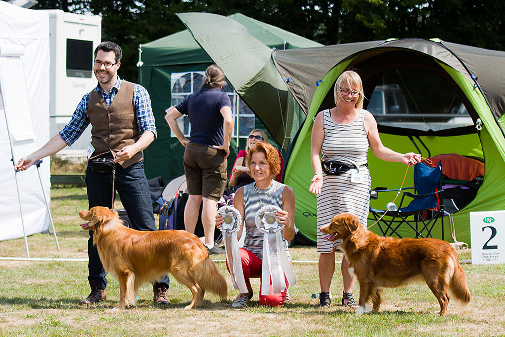 Edison und Stephan posieren zusammen mit Nicky und Birgit fürs Siegerfoto dazwischen die kniende Richterin, die die BOB- und BOS-Rosetten hochhält