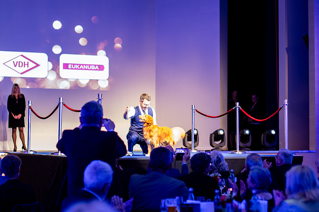 Newton wird von Stephan auf der Bühne hingestellt, im Vordergrund zücken die Menschen ihre Smartphones und fotografieren bzw. filmen das Geschehen