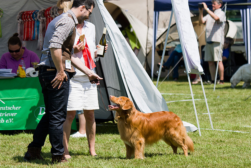 Edison steht vor Stephan und lächelt ihn an, während die Richterin mit dem Preis, einer Flasche Wein, gratuliert